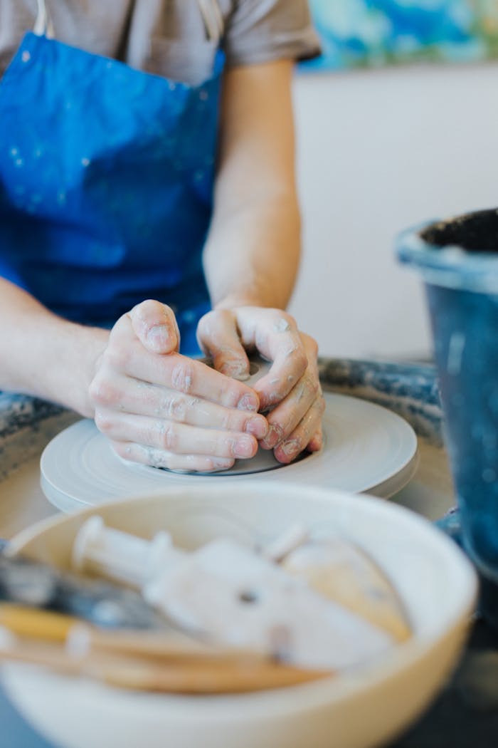 Hands shaping clay on a pottery wheel, capturing the art of handmade ceramics indoors.