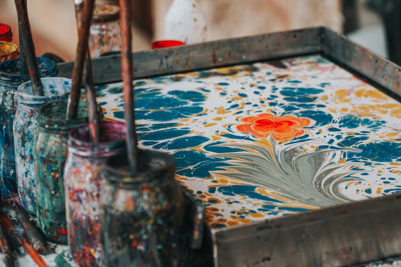 Close-up of colorful marbling art in progress with paint jars and brushes, showcasing vibrant colors and creative expression.