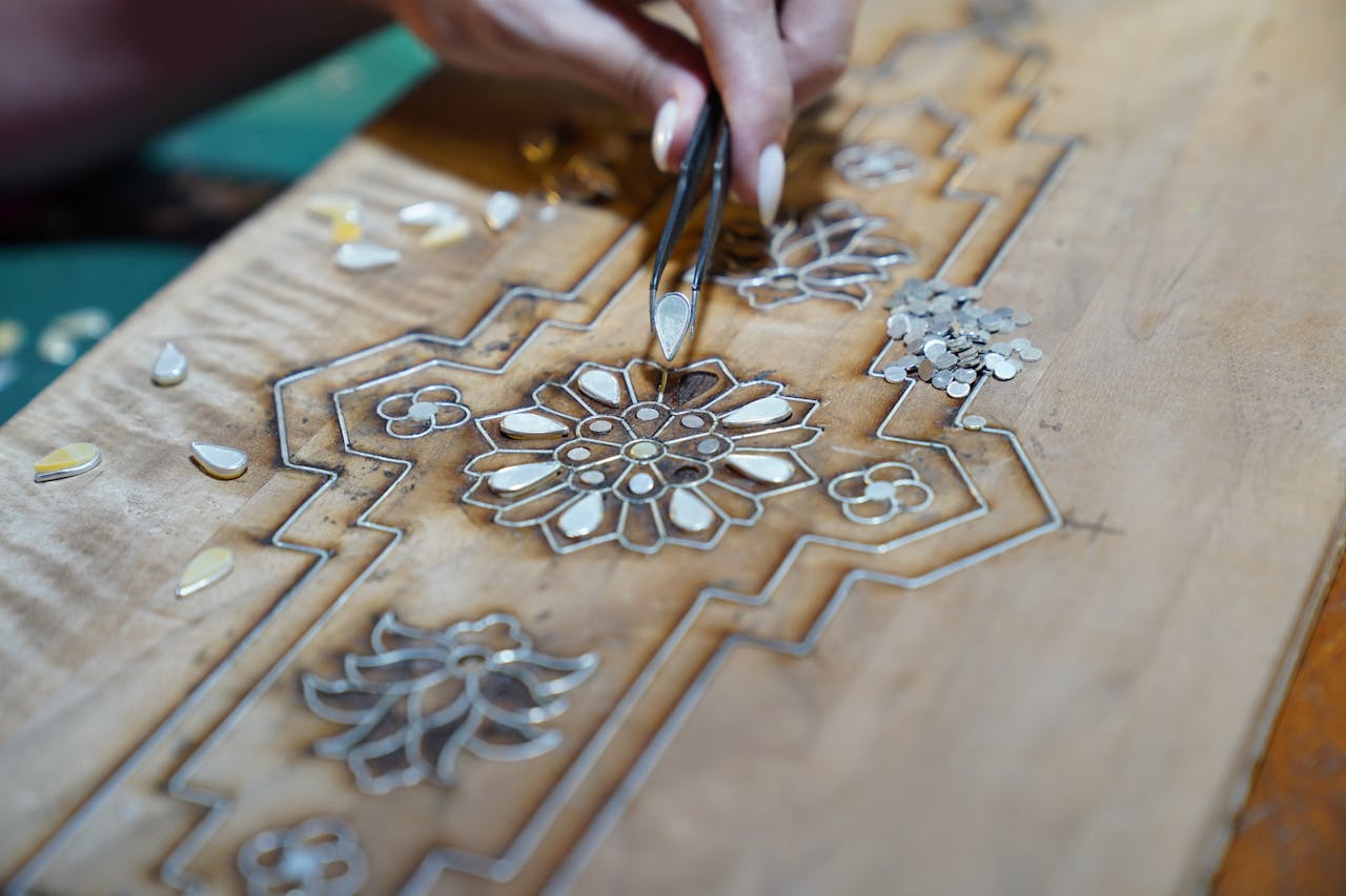 Close-up of a craftsman using tweezers to create detailed wood inlay with floral patterns.